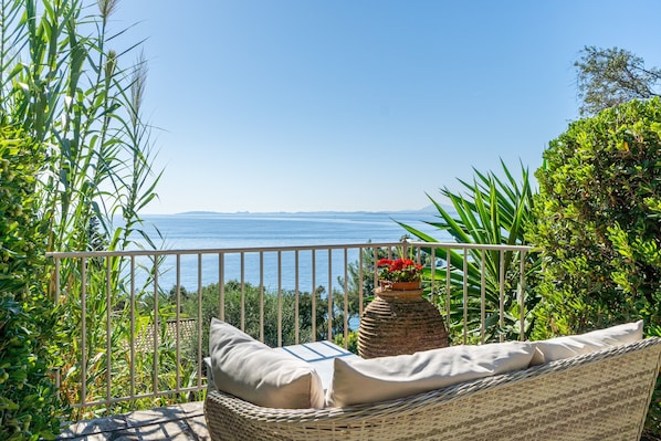 A balcony with wicker furniture, a white railing, and a view of the sea.