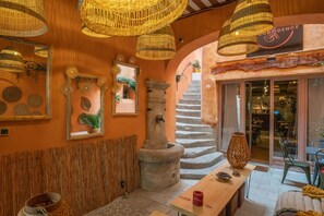 Un interior rústico con pilares de piedra, lámparas de fibra y una escalera que conduce a una puerta de entrada de vidrio.