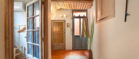 Un pasillo con puerta de madera, suelo de baldosas y un tapete tejido.