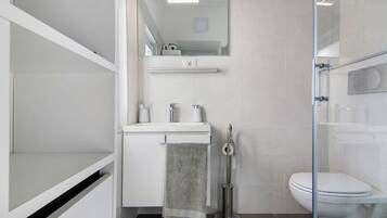 A modern bathroom with a glass shower enclosure, a white sink with a towel, and a toilet.