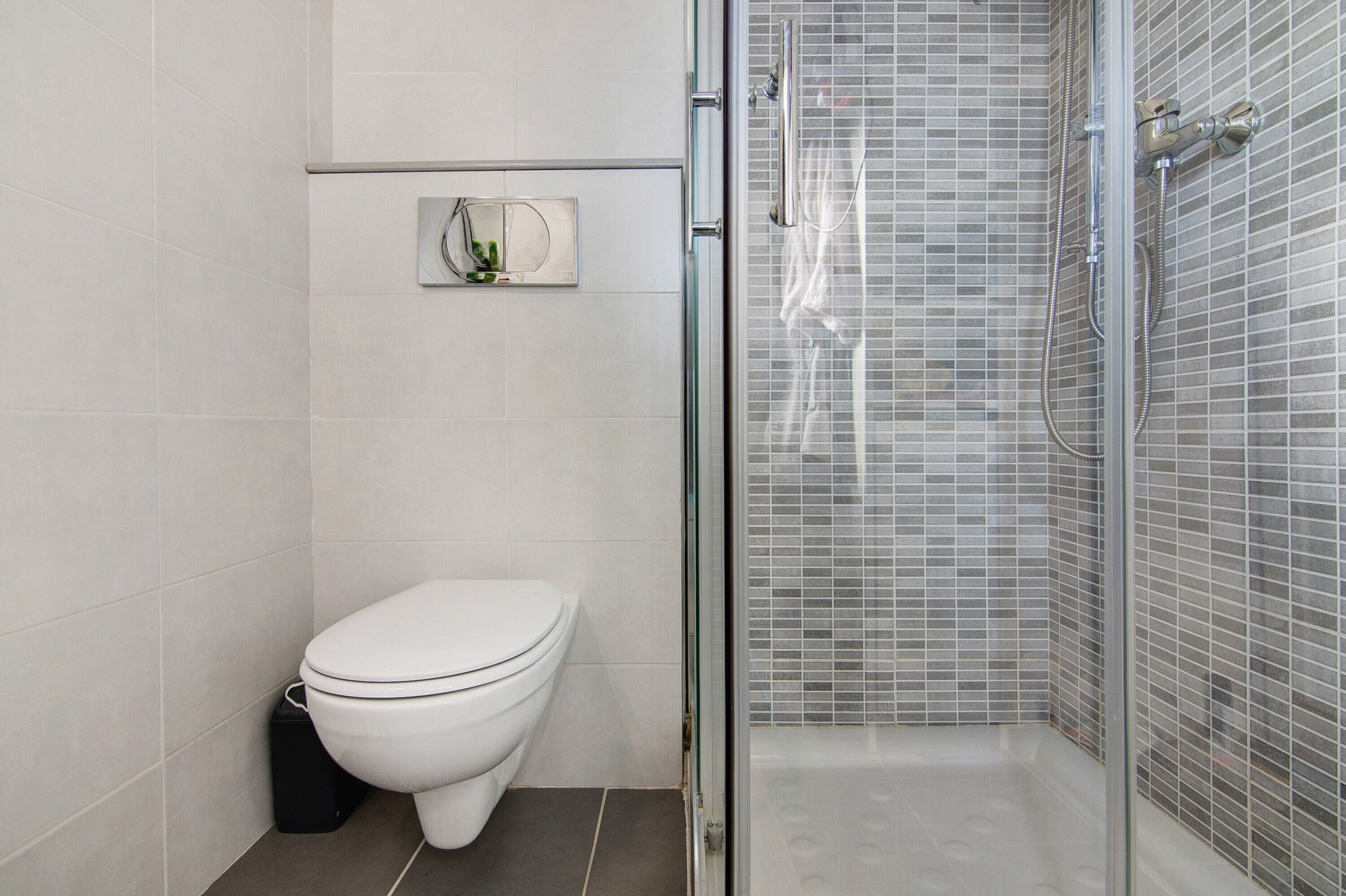 Une salle de bain avec des toilettes, une douche dotée d’une porte en verre et un mur carrelé.
