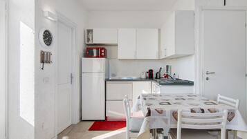 Une cuisine de taille réduite avec des meubles blancs, un micro-ondes rouge et une table à manger recouverte d’une nappe à motifs.