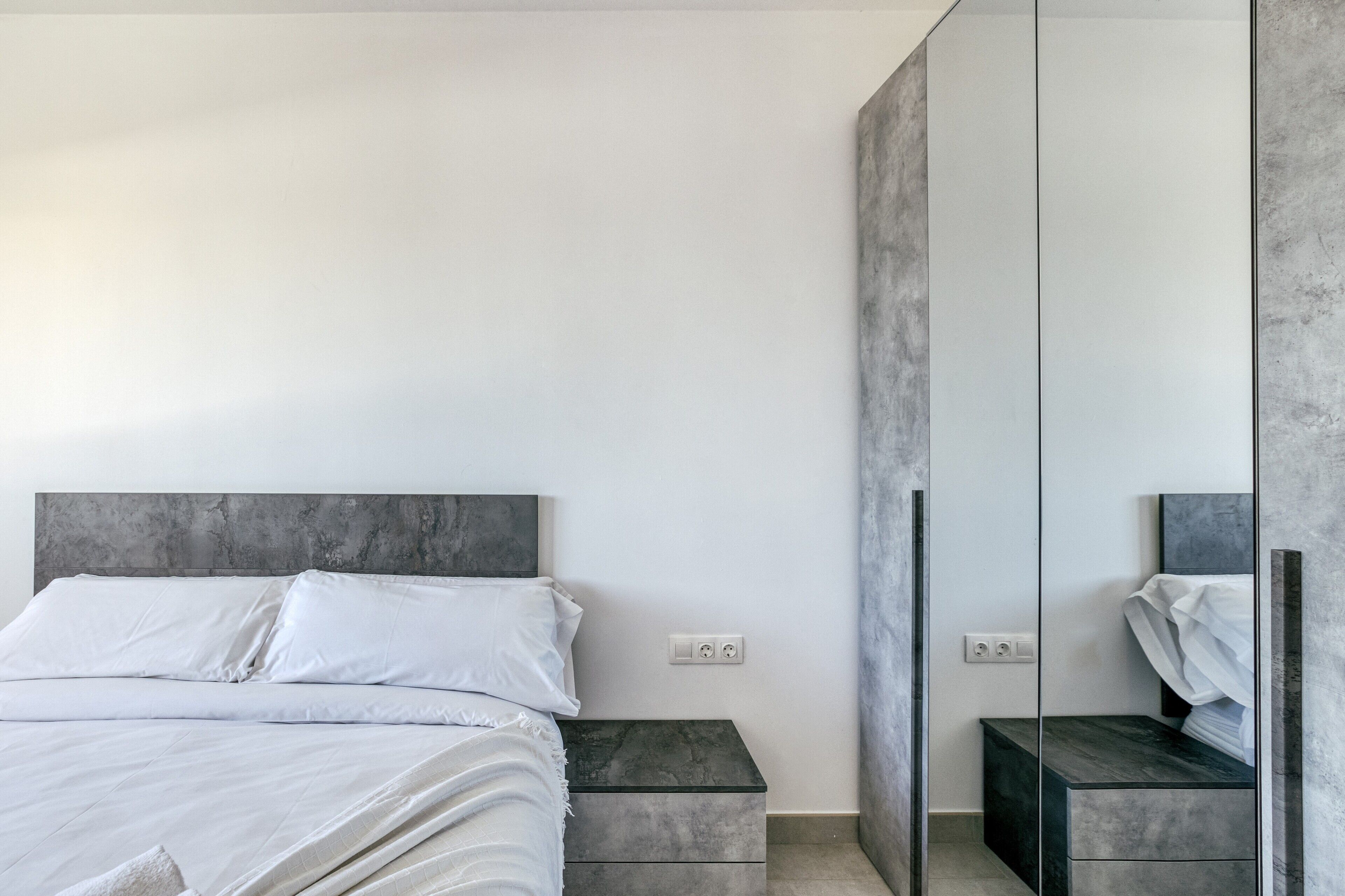 Un dormitorio moderno con cama, mesitas de noche, espejo y armario.