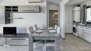 Une cuisine moderne équipée d’un lave-linge intégré, un coin repas avec une table pour quatre personnes et un téléviseur posé sur un meuble.