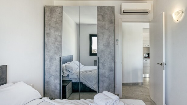Une chambre d’hôtel moderne équipée d’un lit, d’une armoire avec un miroir et d’un coin cuisine visible.