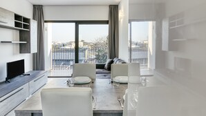 A modern dining area with a table set for two, a sofa, and a TV on a cabinet.