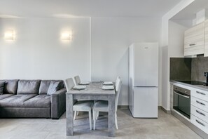 A modern kitchen with a dining table, chairs, a sofa, and a refrigerator.