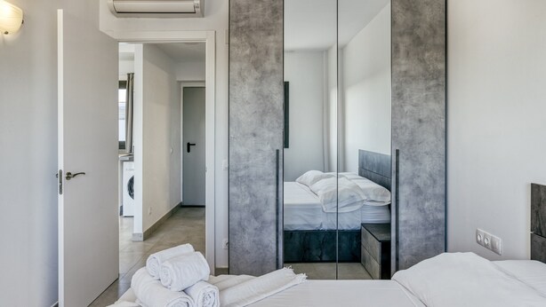 A modern hotel room with a bed, a wardrobe, and a bathroom visible through an open door.