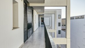 A corridor with a tiled floor, a black railing, and a view of a building with a flat roof.