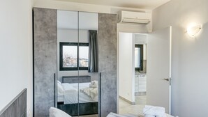 A modern hotel room with a bed, a large mirror, a wardrobe, and a view of the city.