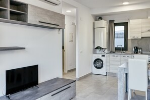A modern kitchen with a built-in washing machine, a dining area with a table and chairs, and a flat-screen TV on a stand.