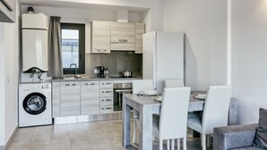 A compact kitchen with a washing machine, a dining table with chairs, and a grey sofa.