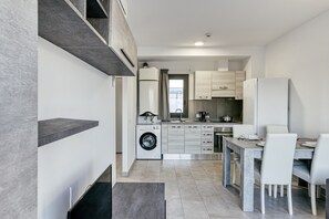 A modern kitchen with a built-in washing machine, a dining area with a table and chairs, and a view of the city through a window.