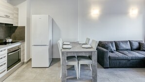 A modern kitchen with a dining table, white refrigerator, and grey sofa.