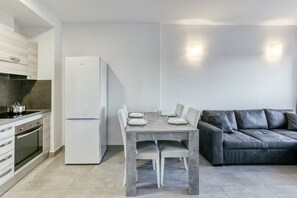 A modern kitchen with a dining table, white refrigerator, and grey sofa.