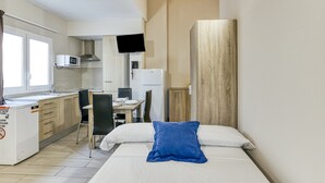 Ein kompakter Raum mit Bett, einer kleinen Küchenzeile, einem Essbereich und einem an der Wand befestigten Fernseher.