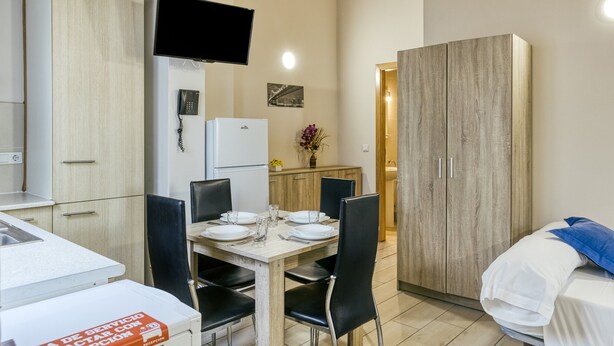 Ein Hotelzimmer mit Essbereich, einem Bett, einem Kleiderschrank, einem Fernseher und einem Telefon.