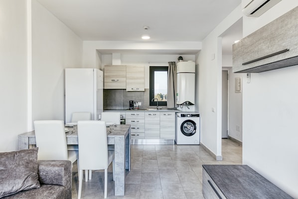 A modern kitchen with a built-in washing machine, a dining area with a table and chairs, and a sofa.