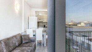 Una sala de estar moderna con un sofá gris, una mesa de comedor con sillas y una cocina al fondo.