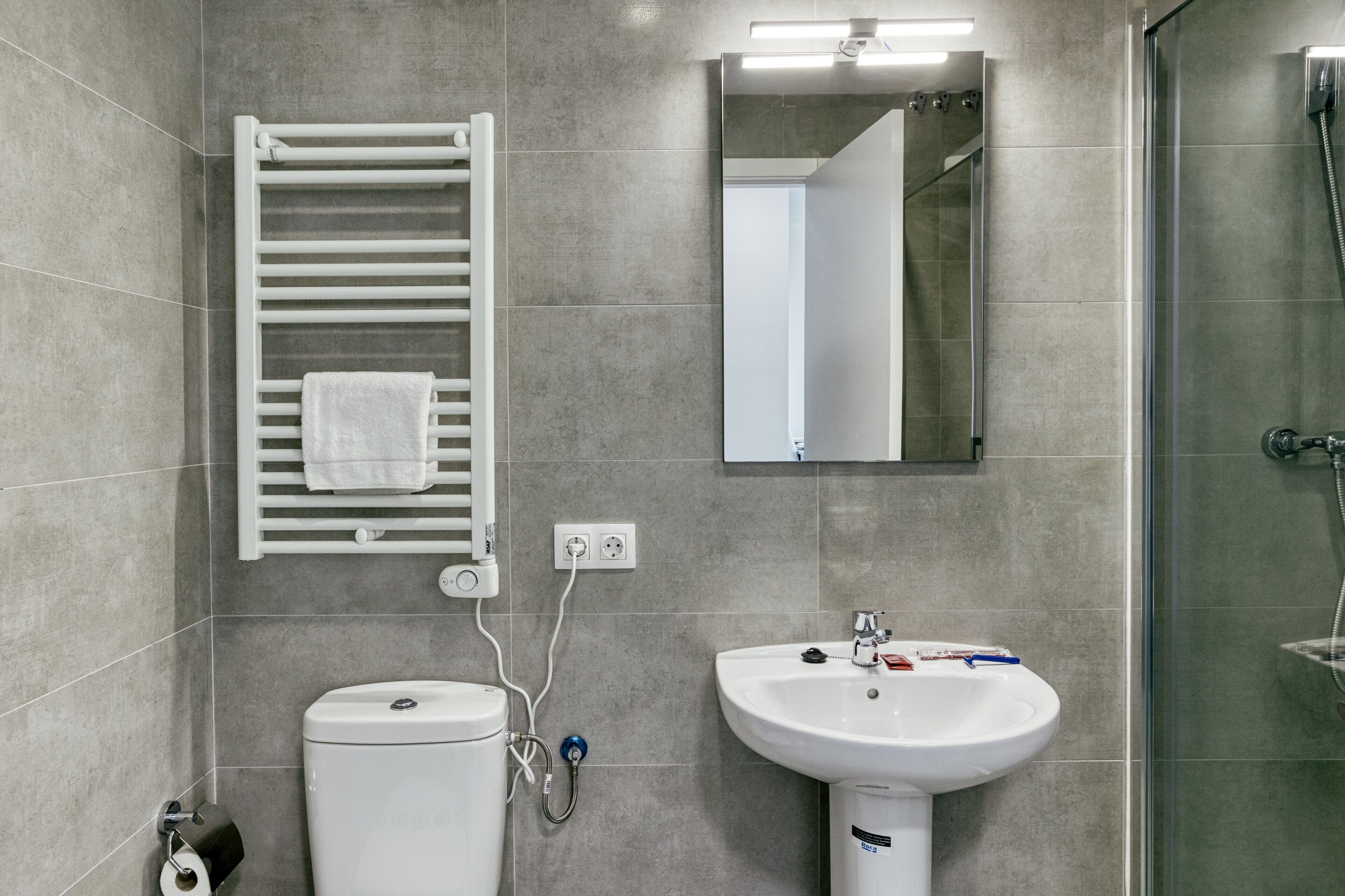 Et moderne badeværelse med toilet, håndvask, håndklædetørre og brusebad.