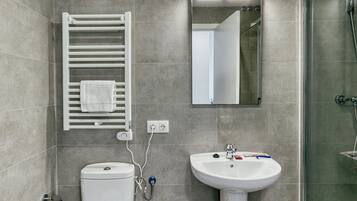Et moderne badeværelse med toilet, håndvask, håndklædetørre og brusebad.