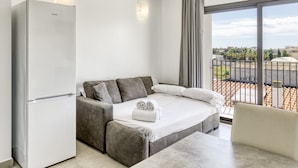 A modern bedroom with a bed, a sofa, a table, and a refrigerator.