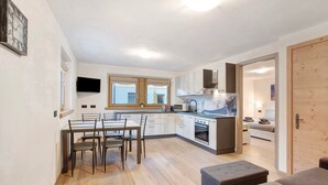 A modern kitchen with a dining area, a TV mounted on the wall, and a wooden door. - Apartment 'Palipert Flowers House' with Mountain View, Shared Garden and Wi-Fi (Livigno)