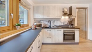 A modern kitchen with wooden cabinets, a built-in oven, a microwave, and a window with a view of the outdoors. - Apartment 'Palipert Flowers House' with Mountain View, Shared Garden and Wi-Fi (Livigno)