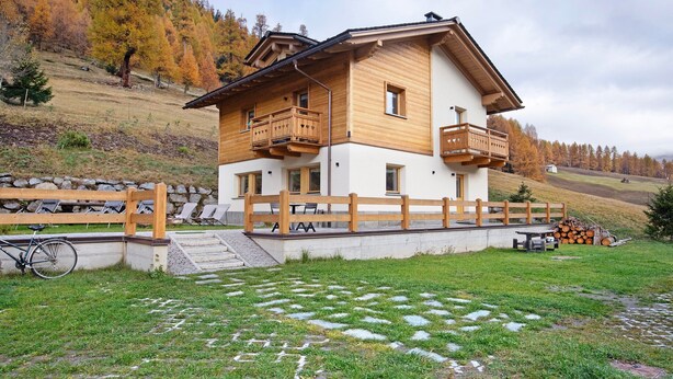 A two-story wooden house with balconies, a stone pathway, and a bicycle. - Apartment 'Palipert Flowers House' with Mountain View, Shared Garden and Wi-Fi (Livigno)