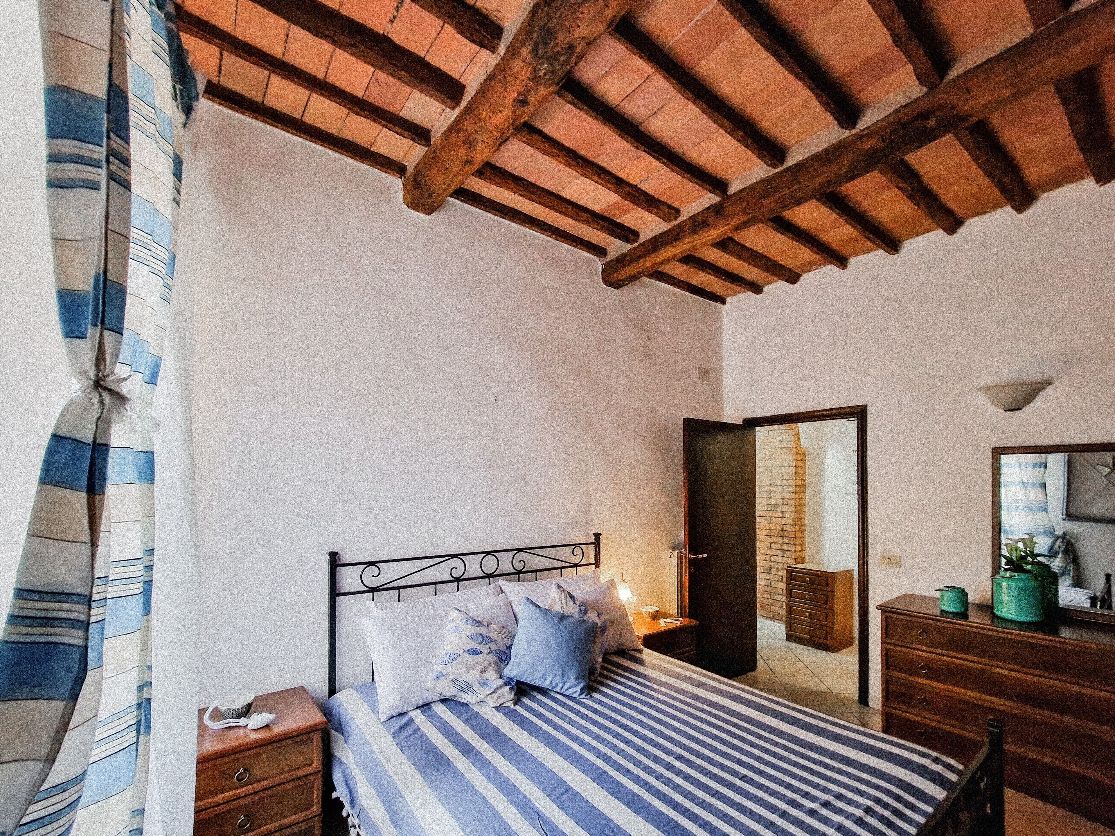 A bedroom with a bed, wooden headboard, a nightstand, a dresser, and a mirror.