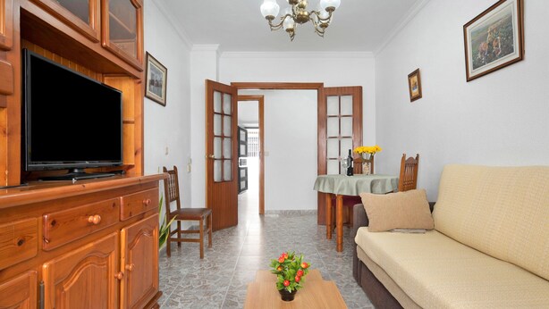 A living room with a television, wooden cabinet, sofa, coffee table, and a dining area with a table and chairs. - Apartment 'Ruz Bajo' for 6 people (Conil)