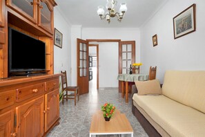 Ein Wohnzimmer mit Fernseher, Holzschrank, Sofa, Couchtisch und einem Essbereich mit Tisch und Stühlen.