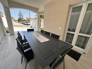 Een terras met een tafel, stoelen, een glazen deur en uitzicht op de straat.