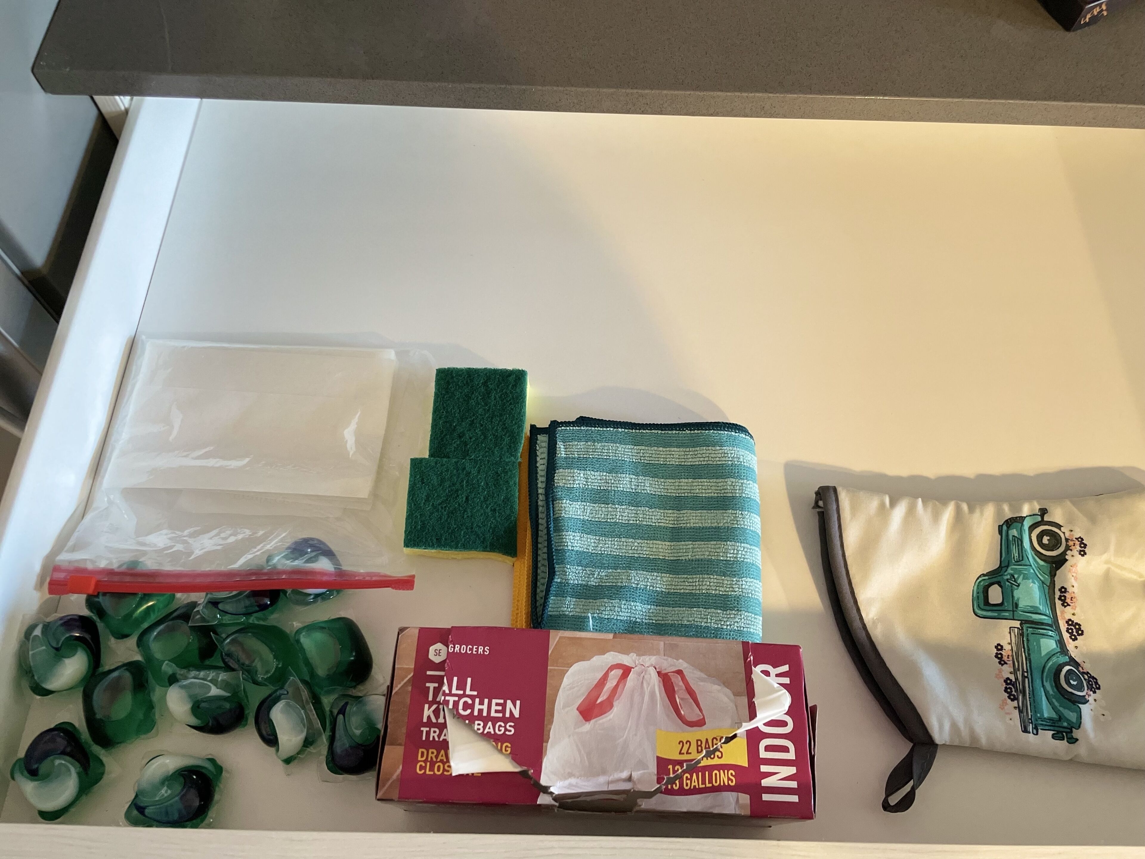 Angolo cottura con diversi oggetti, tra cui una scatola etichettata 'INDOOR', una borsa verde, un panno a righe e un cuscino con un disegno di un camion.