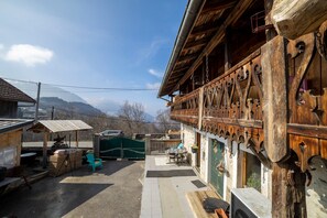 A wooden building with a balcony, a table and chairs outside, and a mountain in the background. - Apartment 'Anna-Purna' with Mountain View, Shared Terrace and Wi-Fi (Arâches-la-frasse)