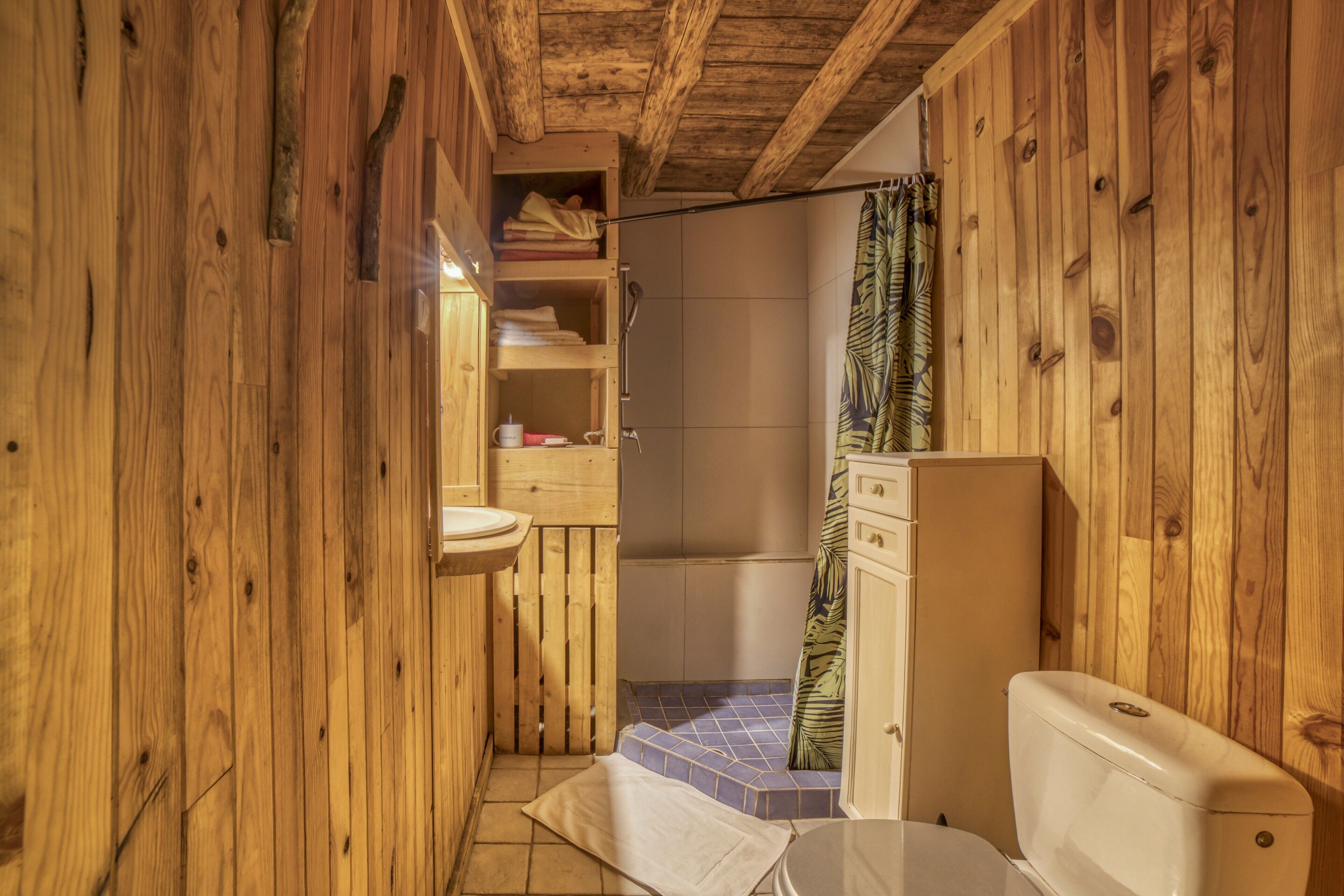 A wooden bathroom with a toilet, sink, and shower.