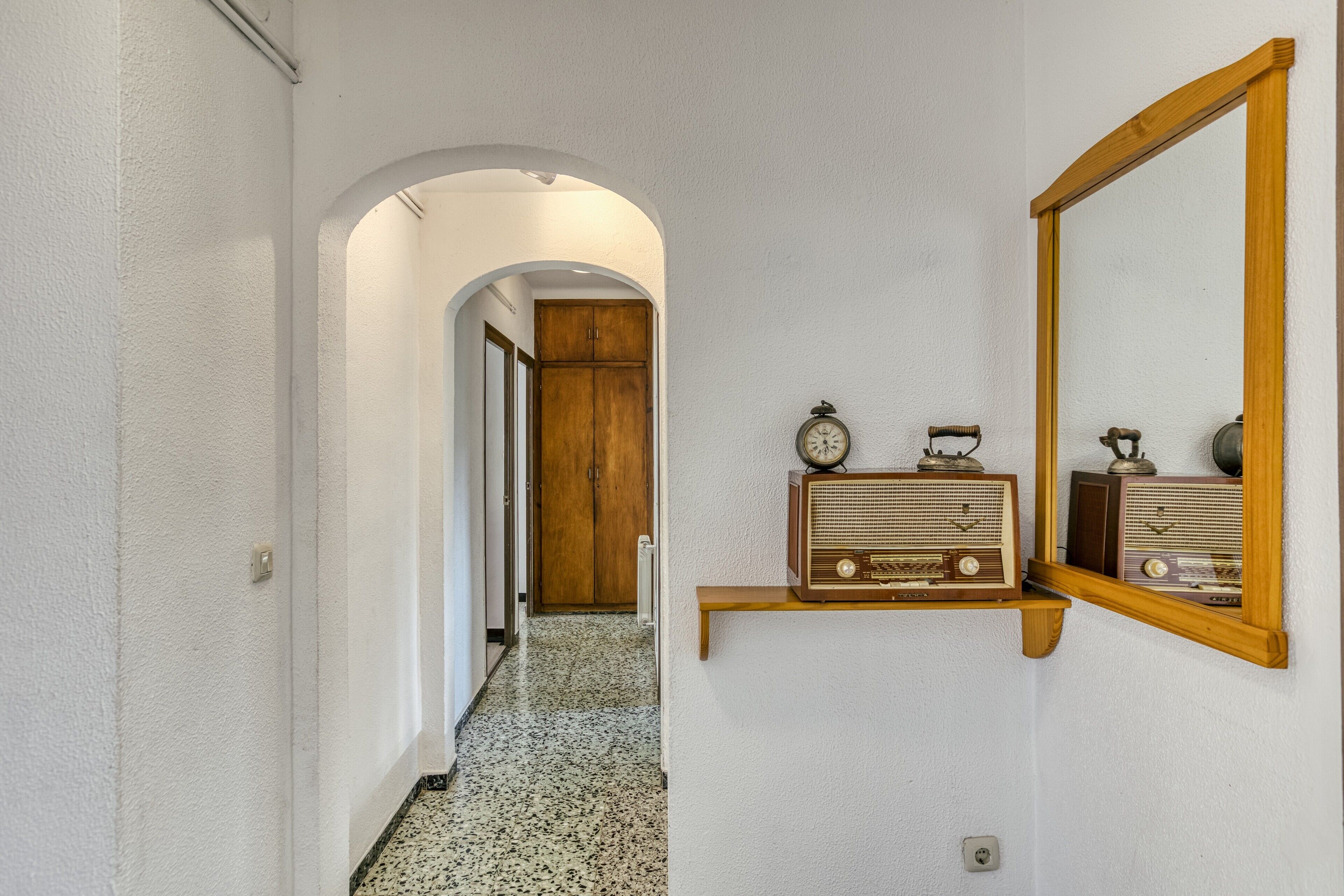 A hallway with a wooden door at the end, a vintage radio on a shelf, and a mirror on the wall.