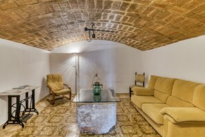 Une pièce avec un plafond en briques, une table basse en verre, un canapé, un fauteuil et une petite table avec une lampe.