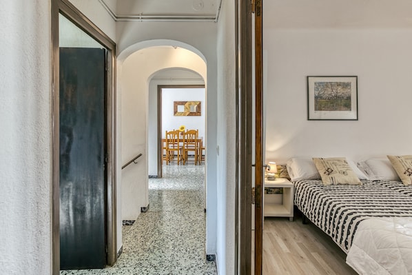 Un couloir mène à une chambre à coucher qui contient un lit, un tableau et un coin repas avec des chaises et une table.