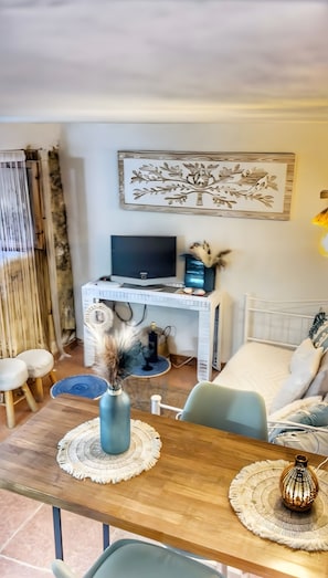 Una sala moderna con una mesa de comedor de madera, un televisor sobre un mueble blanco, un elemento decorativo en la pared y una zona de estar acogedora.