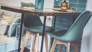 Un coin repas avec une table en bois, deux chaises noires, un vase orné de plumes et un luminaire fixé au mur.