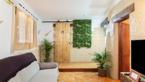 Een woonkamer met een bank, een televisie, een houten deur, een groene muur en potplanten.