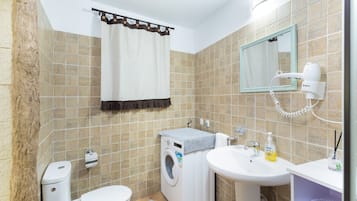 Een badkamer met toilet, wasmachine, wastafel en spiegel.