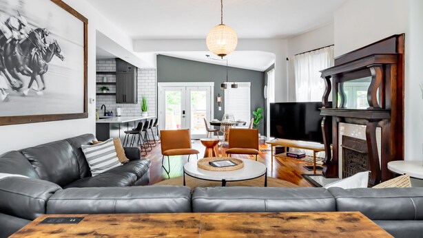 Ett modernt vardagsrum med en lädersoffa, ett soffbord och en tv. Det finns en matplats med stolar och ett bord, och ett kök syns i bakgrunden.