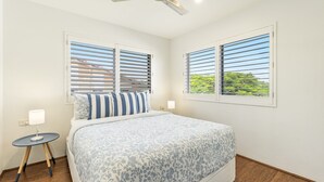 A bedroom with a bed, two windows with blinds, a bedside table with a lamp, and a ceiling fan. - Mingara 4 - Panoramic River, Ocean & Sunset Views - Holiday Yamba (Yamba)