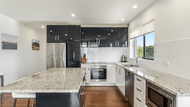 A modern kitchen with black cabinets, stainless steel appliances, and a large island. - Mingara 4 - Panoramic River, Ocean & Sunset Views - Holiday Yamba (Yamba)
