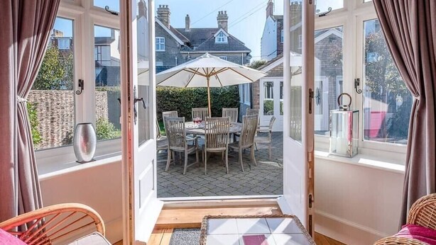 A cozy room with a view of a patio area featuring a table and chairs, a wicker chair, and a small rug. - The White House, Southwold (Southwold)