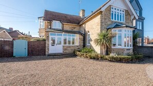 A two-story house with a gravel driveway, a blue gate, and a small garden with a palm tree. - The White House, Southwold (Southwold)