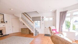 A spacious living room with a wooden floor, a staircase, a fireplace, and a large window with curtains. - The White House, Southwold (Southwold)