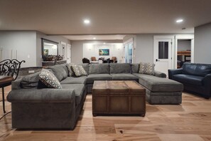 Una sala de estar moderna con un sofá modular, un reposapiés pequeño y un área de comedor al fondo.